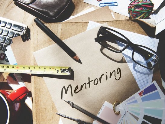 Mentoring Guidance Coaching Training Instruction Concept Stifte, Lineale usw. liegen auf einem Schreibtisch. Auf einem Blatt Papier steht "Mentoring" geschrieben